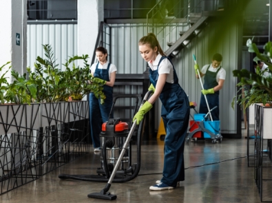 young cleaner vacuuming floor in office near colleagues