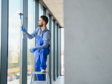 Male janitor cleaning window in office