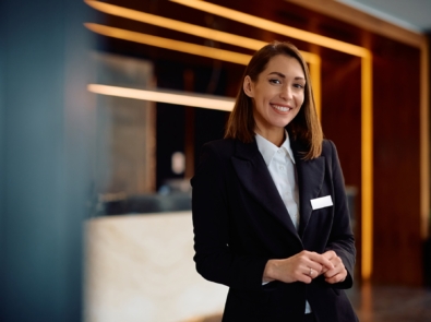 Happy female concierge in hotel hallway looking at camera.