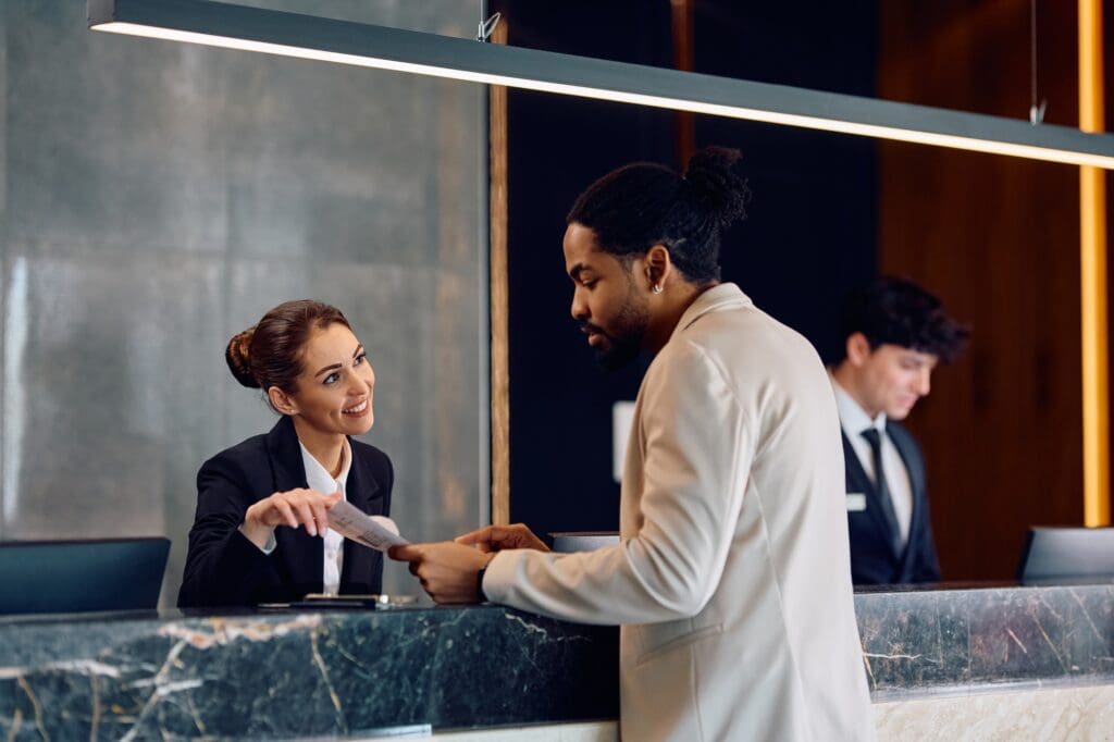 Happy receptionist assisting black male guest who is checking in at the hotel.