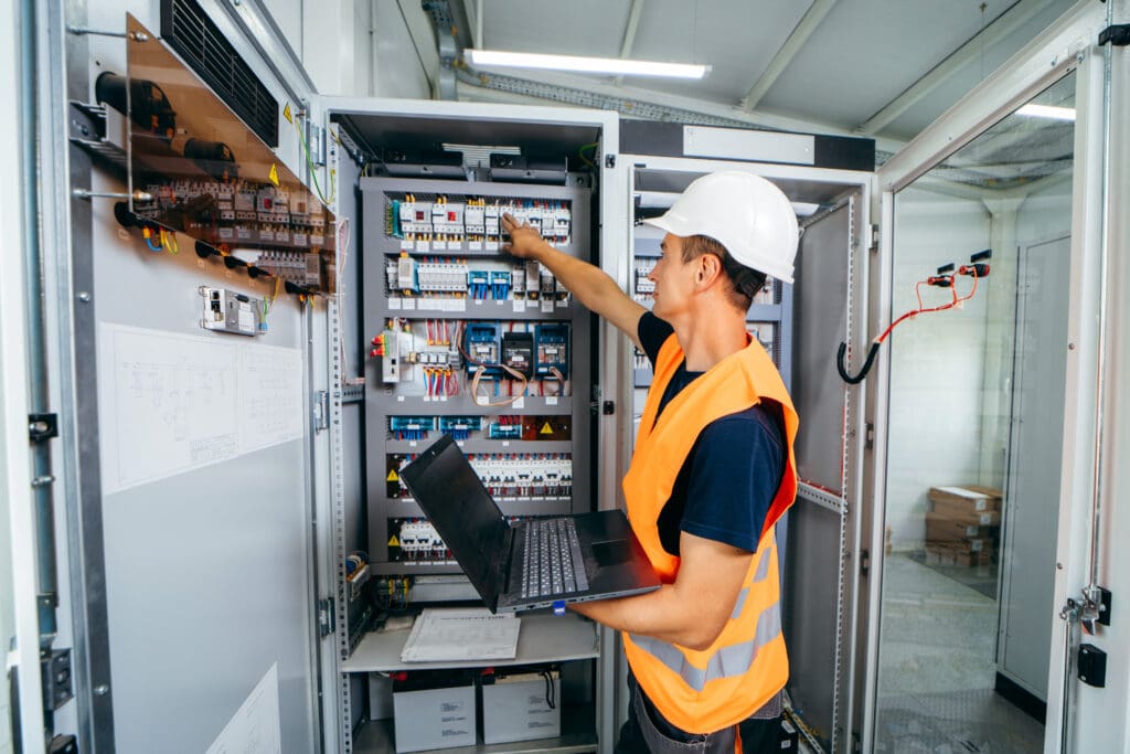 Adult electrician builder engineer testing and screwing equipment in fuse box and repairing of modern electricity power station. Automatic control cabinet